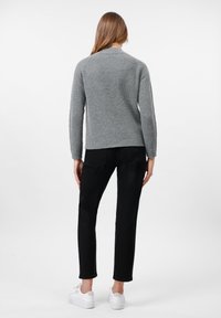 Suéter gris de canalé con cuello redondo y mangas largas, combinado con jeans ajustados negros y zapatillas blancas. Diseño sencillo, sin patrones visibles.
