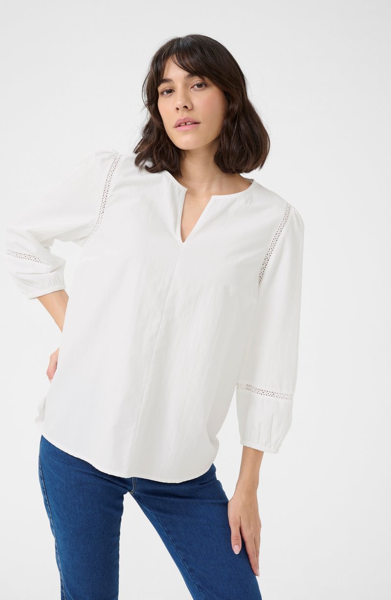 White blouse with a V-neckline and 3/4 puff sleeves. Features lace detailing along the shoulders and sleeves, made of soft cotton fabric.