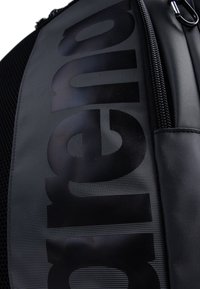 Black backpack featuring a textured surface, large bold branding, a zip closure, and mesh accents for ventilation.