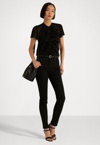 Černá ruflovaná blůza s krátkým rukávem, kombinovaná s černými džínami s vysokým pasem a černými sandály s pásky. Celý outfit doplňuje černá kabelka přes rameno.