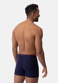 Námořnicky modré boxerky z měkkého materiálu s červeným pruhem na pásku, zobrazené ze zadní strany s hladkou texturou.