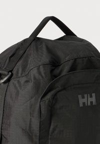 Black backpack made of textured fabric with a structured shape, featuring a top handle and reflective logo detailing.