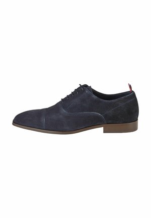 Marineblaue Wildleder-Dressschuhe mit spitzem Zeh, die über dezente Nahtdetails, eine braune Gummisohle und einen kleinen roten Akzent an der Ferse verfügen.