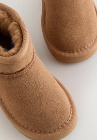 Botine din suede bej cu căptușeală din blană sintetică moale, guler structurat și talpă din cauciuc. Vârf rotunjit și detalii cu cusături contrastante.
