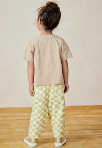 Un t-shirt beige à manches courtes associé à un pantalon à carreaux jaune pâle et marron, offrant une coupe décontractée et des poches, complète la tenue.