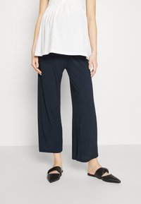 Námořnické široké kalhoty vyrobené z měkké tkaniny, s uvolněným střihem a hladkou strukturou, doplněné černými pointed-toe pantoflemi.