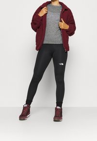 Burgundy fleece jacket over a gray t-shirt, paired with black leggings and burgundy hiking boots featuring gray accents and metal eyelets.