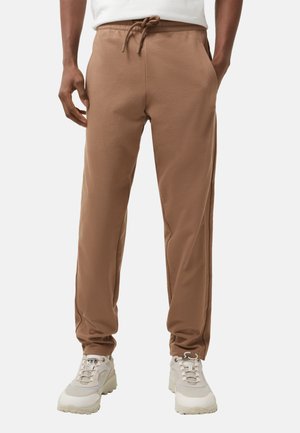 Brune sweatpants lavet af blødt materiale med snoretræk i taljen, slim fit og sidelommer. Matcher med lyse atletiske sko.