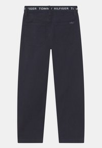 Granatowe spodnie o prostym kroju, z podwójnymi tylnymi kieszeniami i paskiem z nazwą "TOMMY HILFIGER" w białych literach.