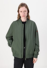Olijfgroene bomberjack met een ritssluiting aan de voorkant, ribgebreide manchetten en zijzakken. Bevat een logopatch op de linkerarm. Gladde textuur.