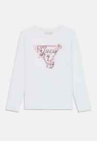 Hvitt langermet skjorte med rosa blomstrete trekantdesign og "Guess Los Angeles?" logo plassert midt på forsiden.
