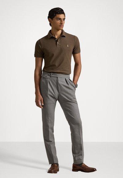 Polo marron avec col, pantalon plissé gris, chaussures en cuir marron et montre. Le tissu est lisse avec une coupe ajustée.