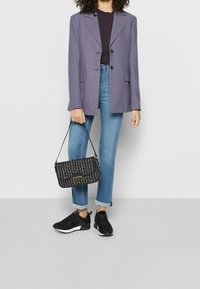 Blazer a cuadros en púrpura y azul, llevado sobre una camiseta oscura. Jeans azul claros, zapatillas negras y un bolso de mano con un patrón en blanco y negro.