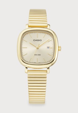 Montre Casio en or avec un boîtier carré, un cadran texturé doré et un affichage de la date, équipée d'un bracelet métallique doré côtelé. Résistante à l'eau jusqu'à 50 mètres.