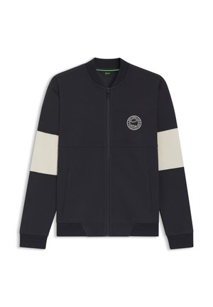 Navy zip-up jacket with cream horizontal stripes on sleeves, ribbed cuffs, and a round logo on the chest. Made from soft fabric.