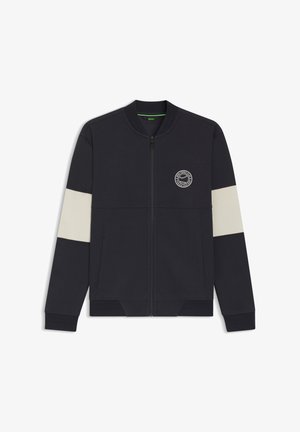 Giacca con zip blu navy con strisce orizzontali color crema sulle maniche, polsini a coste e un logo rotondo sul petto. Realizzata in tessuto morbido.