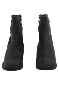 Botas de ante negras hasta el tobillo con punta afilada, costuras verticales y cremalleras laterales. El tacón tiene una forma curva para una silueta ajustada.