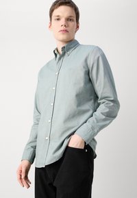 Lichtblauw button-up shirt van textuurstof, met een kraag, witte knopen en een klein logo. Gecombineerd met zwarte broek.