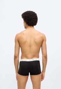 Μαύρα μποξεράκια με λευκή μέση που φέρει το λογότυπο "TOMMY HILFIGER". Ομαλό ύφασμα, εφαρμοστή σχεδίαση, απεικονίζεται από πίσω.