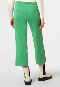 Pantaloni larghi verdi con vita elasticizzata, dotati di due tasche posteriori, abbinati a stivali alla caviglia crema e neri. Tessuto dalla texture liscia.