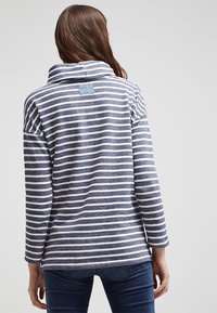 Randig tröja i marinblått och vitt, med hög krage och en detalj på ryggen. Mjuk kvalitet med avslappnad passform och långa ärmar.