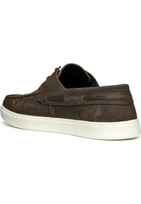 Zapato de cuero marrón con un acabado texturizado, suela de goma blanca, punta redondeada y detalles de costura minimalistas. La vista lateral muestra un diseño sencillo.