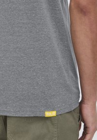 Grå kortærmet t-shirt lavet af blødt stof. Har et gult logo-tag "ISOLID" på kanten. Bæres med khaki shorts.