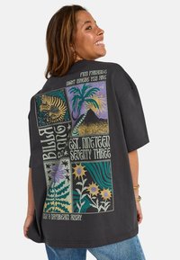 T-shirt nera oversize con stampe grafiche colorate di elementi naturali, testo e motivi geometrici sul retro. Maniche corte e vestibilità rilassata.
