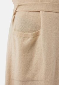 Beige ullplagg med texturerad yta, som har en sidficka och ett matchande bälte för att knyta ihop.