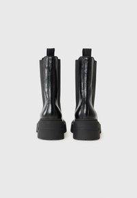 Bottes noires à bout carré avec une semelle épaisse et une finition en cuir souple, vues de l'arrière, mettant en valeur leur design élégant et leur structure.