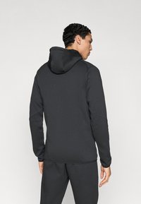 Σκούρο γκρι φούτερ με κουκούλα και απαλή υφή, που διαθέτει μακριά μανίκια, ραφές στους ώμους και μινιμαλιστικό σχέδιο.