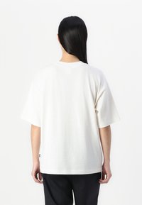 White cotton t-shirt with a relaxed fit, dropped shoulders, and short sleeves. Features a small logo tag at the hem. Plain design, no patterns.