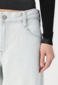 Jeans de mezclilla azul claro con un corte relajado, que presentan un cierre de botón, bolsillos frontales y una cinturilla texturizada. Superficie lisa con costuras mínimas.