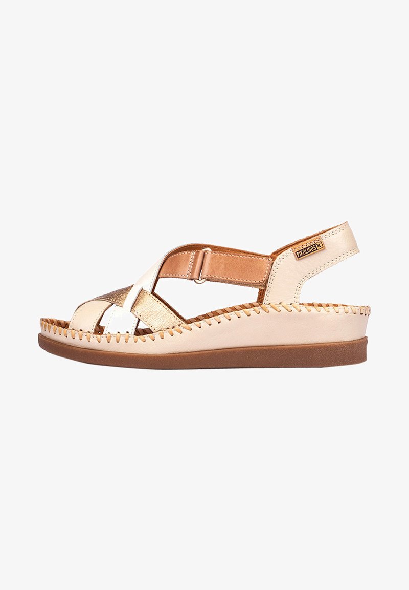 Sandalia de cuero beige y dorado con correas cruzadas, correa de tobillo ajustable y suela texturizada. Detalles cosidos a mano alrededor de los bordes.