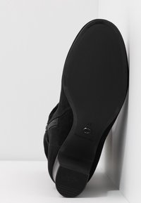Bottine en suede noir avec fermeture éclair, talon bas, et semelle en caoutchouc lisse. Présente un panneau latéral texturé et un bout arrondi.