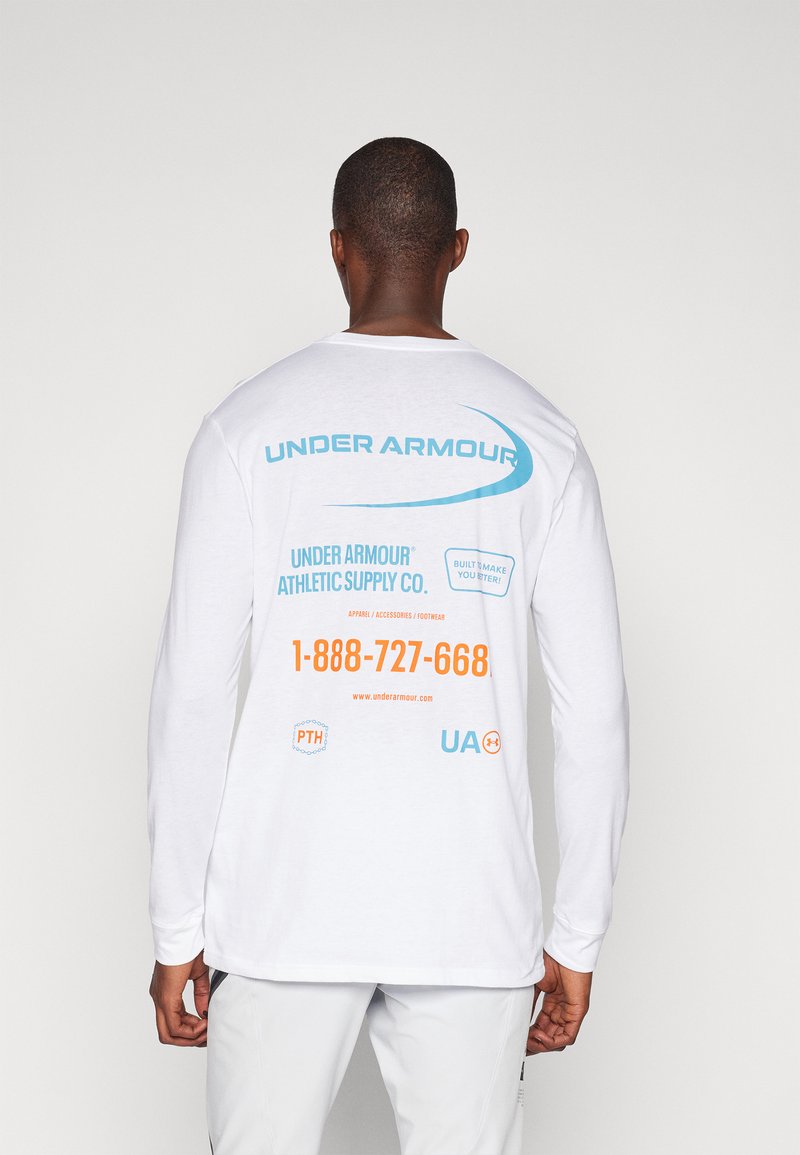 Valge pikkade varrukatega särk, mille seljal on sinise ja oranži tekstiga "Under Armour" logo koos kontaktandmete ja muude brändingute detailidega.