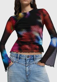 Top lung negru cu mânecă lungă, prezentând un model abstract colorat, cu un finisaj texturat și tiv volanat. Asortat cu blugi din denim albastri cu talie înaltă.