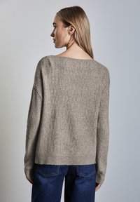 Ljus beige ribbad tröja med vid halsringning och långa ärmar, med en avslappnad passform och mjuk textur, kombinerad med mörkblåjeans.