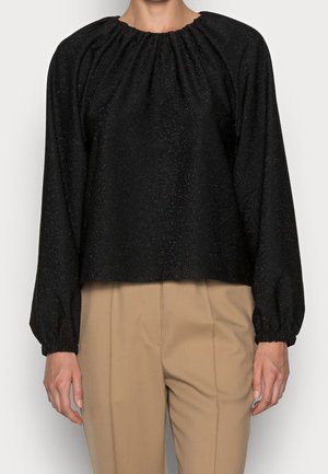 Zwarte blouse met lange mouwen, met een gegarnekte halslijn en manchetten, gedragen met beige broek met hoge taille.