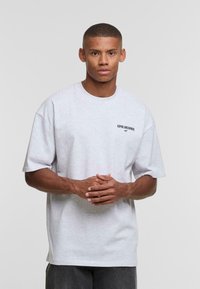 T-shirt in cotone grigio, maniche corte, collo rotondo. Presenta il testo nero "ASPIRE AND ACHIEVE" sul lato sinistro del petto. Vestibilità rilassata.