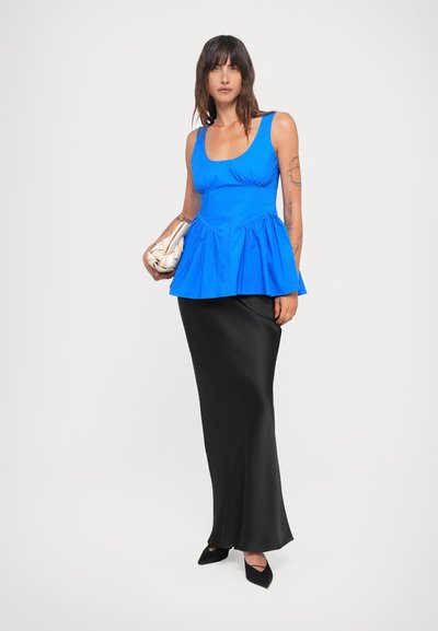 Blue peplum top with scoop neckline, paired with a floor-length black satin skirt. Model holds a textured cream handbag and wears black heels.
