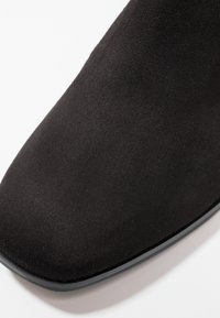 Gros plan de l'avant carré en daim noir d'une chaussure avec une surface lisse légèrement texturée et un bord de semelle fin.