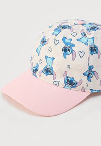 Καπέλο με ελαφρύ μπεζ ύφασμα που έχει επαναλαμβανόμενο μοτίβο με καρτούν χαρακτήρες, ροζ καμ πύλη κορυφή και απαλή υφή. Διακριτά σχήματα καρδιών στο σχέδιο.