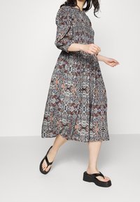 Mekko, jossa on kukkakuosi, ryysypintainen yläosa, puffihihat ja polven pituinen helma. Valmistettu kevyestä kankaasta sinisen, punaisen ja kerman sävyissä.