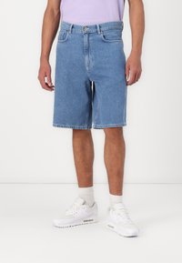 Denim shorts with a loose fit, light blue color, five pockets, and frayed hems, paired with white sneakers and light socks.