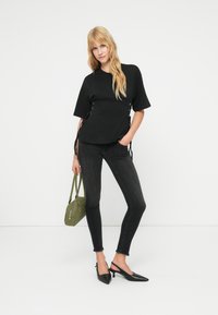 Μαύρο τοπ με κοντά μανίκια και κορδόνια στο πλάι, σε συνδυασμό με σκούρα στενά τζιν και μαύρες μυτερές γόβες. Κρατάει μια μικρή πράσινη τσάντα χειρός.