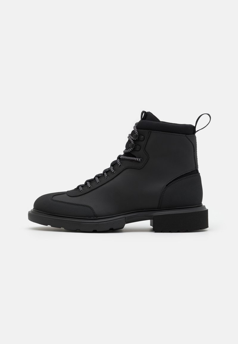 Bottine noire à lacets avec col rembourré, languette au talon et semelle épaisse en caoutchouc crantée, vue de côté extérieur sur fond blanc.