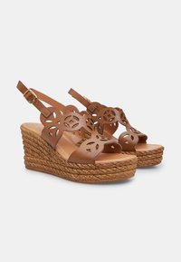 Sandales compensées marron avec un design floral découpé, tige en cuir et talon en jute tressé. Fermeture à boucle et bout ouvert. Semelle texturée.
