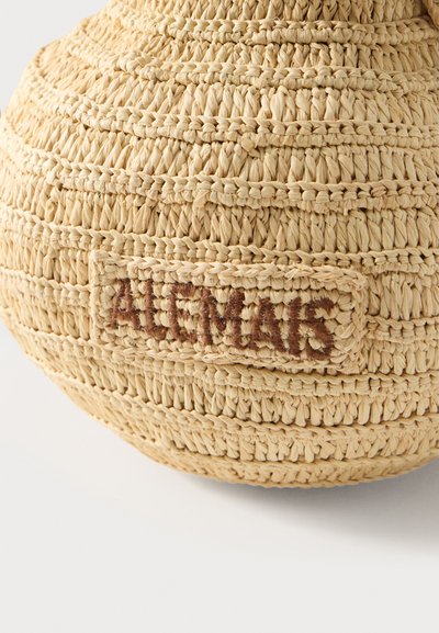 Φυσικό πλεκτό ψάθινο καπέλο με ραμμένη ορθογώνια ετικέτα που φέρει το όνομα της μάρκας "ALCIMAS" με καφέ κλωστή.