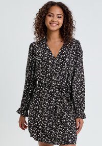 Robe noire avec imprimé floral blanc, col en V, manches longues et taille cintrée. Tissu doux avec une texture légère et fluide.
